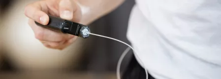 Insulinpumpe Eine Person hält eine Insulinpumpe in der Hand. Der Schlauch verschwindet unter dem Shirt.