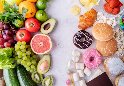 Auf der linken Seite liegen gesunde Lebensmittel wie Obst und Gemüse, auf der rechten liegen Naschwaren und Gebäck