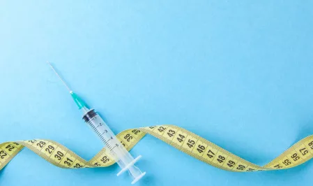 Auf einem blauen Hintergrund liegen eine Einmalspritze und ein gelbes Ma&szlig;band. 