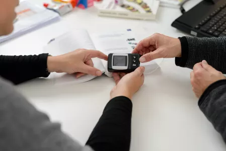 Diabetes-Technik Besprechung Zwei Personen schauen gemeinsam auf das Steuerungsgerät einer Insulinpumpe und besprechen die angezeigten Informationen