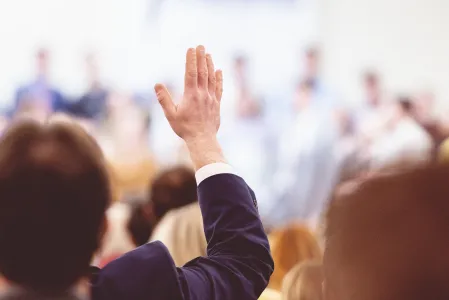 Personengruppe bei einer Versammlung, Mann im Anzug hebt seine Hand