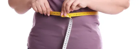 BMI Eine Frau hält ein Maßband um ihre Taille.