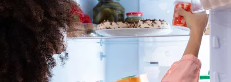 Heißhunger Eine Frau greift in einen Kühlschrank und holt etwas heraus.