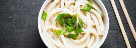 Udon-Nudeln Udon Nudeln in Suppe in einer weißen Schüssel. Daneben liegen Essstäbchen