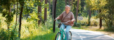 Eine Frau in den f&uuml;nfzigern F&auml;hrt mit einem Fahrrad durch den Wald.