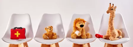 Stofftiere und Erste-Hilfe-Koffer auf einer Reihe von St&uuml;hlen