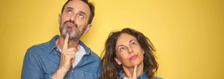 Geschlechtsunterschiede Ein Mann und eine Frau vor einer gelben Wand. Sie schauen nachdenklich.
