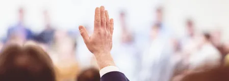 Person meldet sich mit Handzeichen in einer Vortragssituation