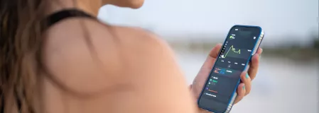 Blick &uuml;ber die Schulter einer jungen Frau auf ein Smartphone, auf dem verschiedene Kurven zu sehen sind
