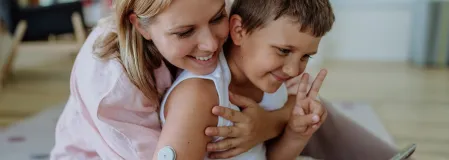 Kinderspendenprojekte Mutter, die ihren Sohn mit Diabetes umarmt und zusammen ins Handy schauen