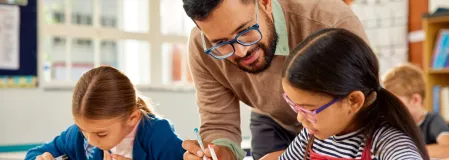 Lehrer erkl&auml;rt einer Sch&uuml;lerin etwas, eine zweite Sch&uuml;ler sitzt daneben