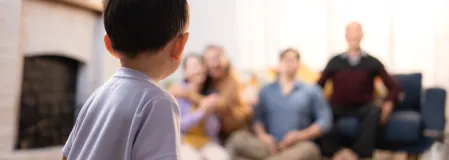 Ein Kind schaut auf seine Familie, die verschwommen im Hintergrund zu sehen ist.