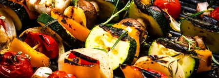 Gemüsspieße Gemüsespieße auf einem Grill. Tomaten, Zucchini, Paprika, Ziebel und Pilze sind auf dem Spieß zu finden. Auf dem Grill liegt außerdem eine Knoblauchknolle.