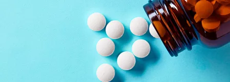 Orale Antidiabetika Eine braune Arzneiflasche liegt offen auf blauem Hintergrund. Weiße Tabletten fallen heraus und liegen vor der Flasche.