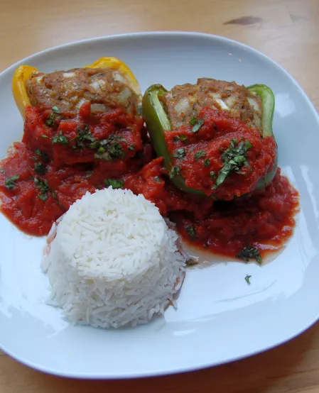 Gefüllte Paprikaschote mit Reis Eine gelbe und eine grüne mit Hack gefüllte Paprika mit Tomatensoße und Reis als Beilage