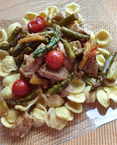 Pasta mit Spargel Auf einem Glasteller ist Pasta mit grünem Spargel, Tomaten, und Hähnchen angerichtet