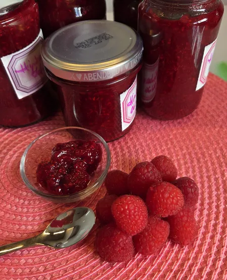 frische Himbeeren neben einer Schale mit Himbeermarmelade und mehreren Gl&auml;sern mit Marmelade