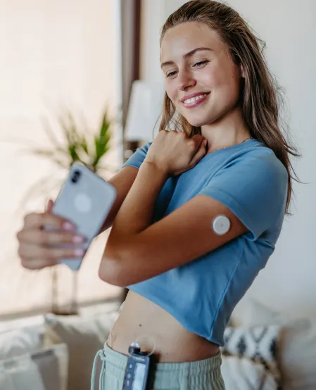 CGM-System Eine junge Frau macht ein Selfie und hält ihren Sensor auf dem Arm in die Kamera in