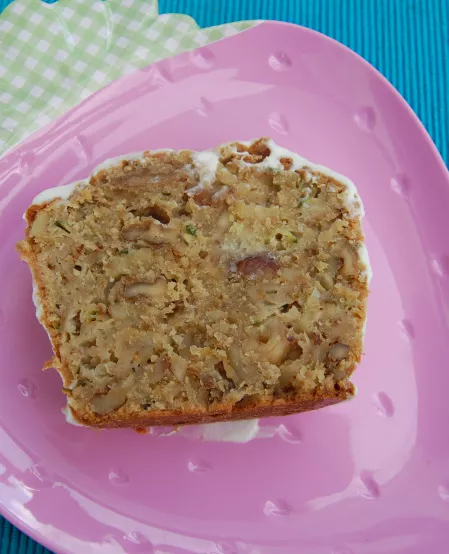 Süßer Zucchinikuchen Ein Stück Zucchinikuchen auf einem rosa Teller in Form einer Erdbeere. Auf dem Stück Kuchen ist eine weiße Glasur.