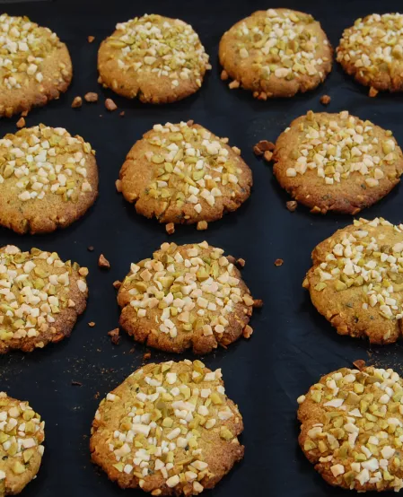 Mandelcookies Die Mandelcookies liegen auf einem schwarzen Untergrund. Sie sind mit Mandel- und Pistazienstückchen garniert.