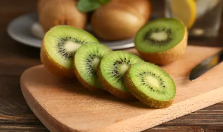 Kiwi Eine aufgeschnittene Kiwi auf einem Holzbrett im Vordergrund und im Hintergrund weitere ganze Kiwis