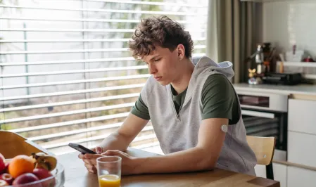 Junge mit Diabetes sitzt am Tisch und schaut in sein Handy