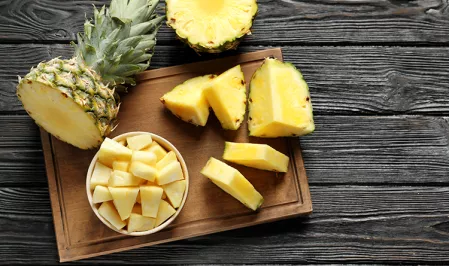 Eine Ananas liegt aufgeschnitten auf einem Holzbrett