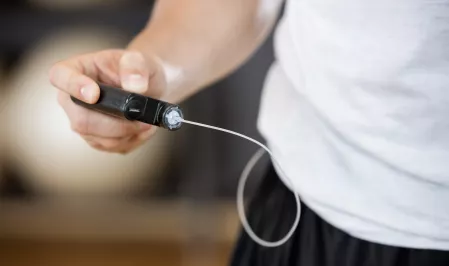 Insulinpumpe Eine Person hält eine Insulinpumpe in der Hand. Der Schlauch verschwindet unter dem Shirt.