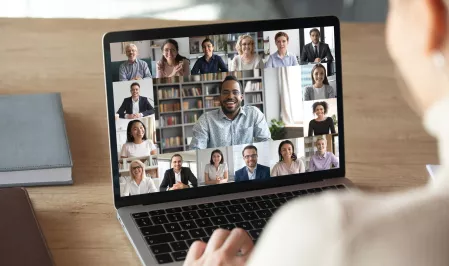 Webinar Person vor einem Laptopbildschirm, auf dem viele einzelne Menschen im Portrait zu sehen sind