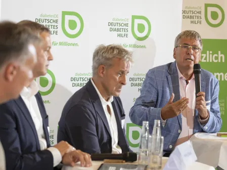 FC Diabetologie vs. FC Bundestag 2025: Dr. Kröger spricht, neben ihm sitzt Pierre Littbarski
