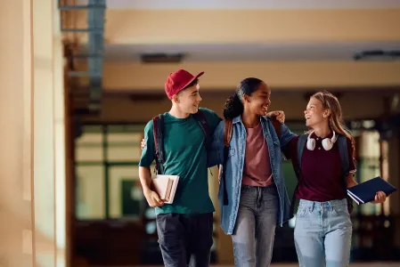 drei Jugendliche halten sich an der Schulter und lachen sich an 