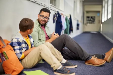 Junge sitzt neben seinem Lehrer auf dem Boden