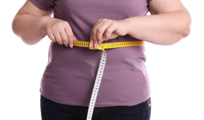 Eine Frau hält ein Maßband um ihre Taille.