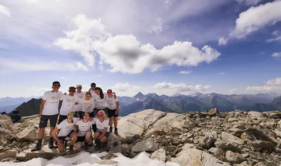 Eine Gruppe von Menschen auf einem Berggipfel, im Hintergrund Ausblick auf die Alpen