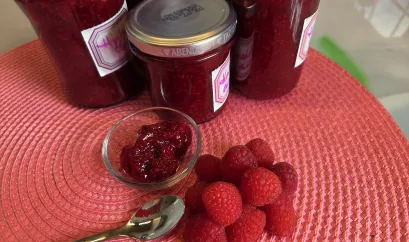 frische Himbeeren neben einer Schale mit Himbeermarmelade und mehreren Gl&auml;sern mit Marmelade