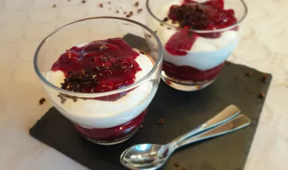 Das Schwarzwälder Kirsch-Dessert ist in zwei Gläser geschichtet, unten dunkle Pumpernickelbrösel, dann Kirschkompott, darüber Quark und oben etwas Kompott garniert mit etwas Brösel.