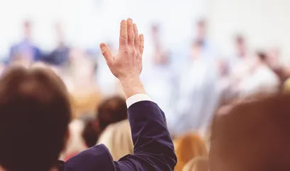 Personengruppe bei einer Versammlung, Mann im Anzug hebt seine Hand