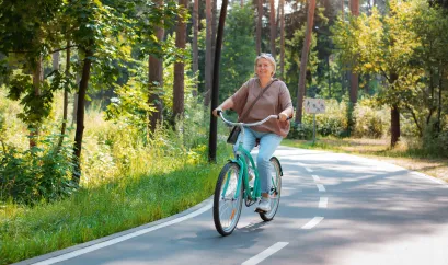 Eine Frau in den fünfzigern Fährt mit einem Fahrrad durch den Wald.