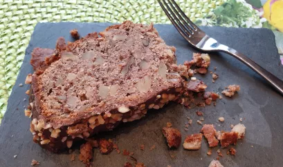 Ein Stück dunkler Nusskuchen liegt auf einem grauen Brett