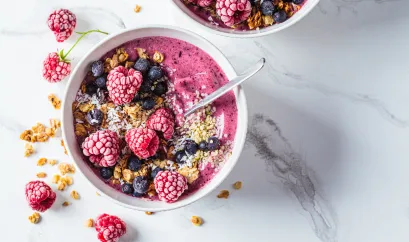 eine Bowl mit pinkem Joghurt, Haferflocken und gefrorenen Himbeeren und Blaubeeren