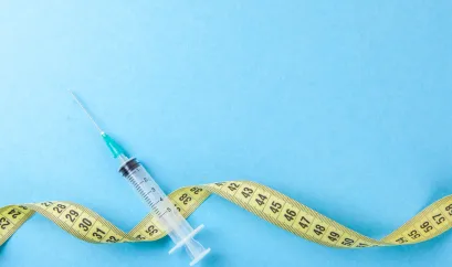 Auf einem blauen Hintergrund liegen eine Einmalspritze und ein gelbes Maßband. 