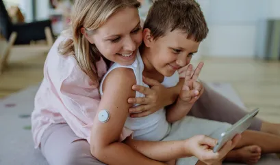 Mutter, die ihren Sohn mit Diabetes umarmt und zusammen ins Handy schauen