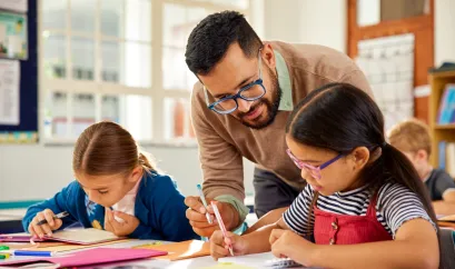 Lehrer erkl&auml;rt einer Sch&uuml;lerin etwas, eine zweite Sch&uuml;ler sitzt daneben