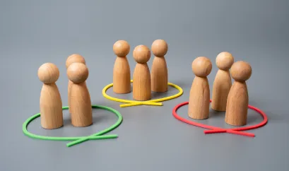 Holzfiguren sind in drei Gruppen aufgeteilt aufgestellt. Um jede Gruppe ist ein farbiges Band.