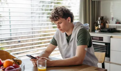 Junge mit Diabetes sitzt am Tisch und schaut in sein Handy