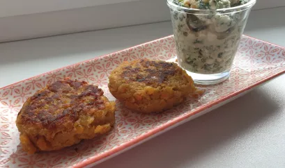 Auf einer länglichen Schale sind 2 Linsenbratlinge angerichtet. Der Kräuterdip steht in einem kleinen Glässchen daneben.