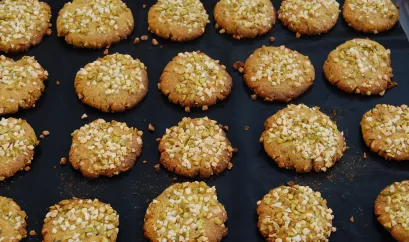 Die Mandelcookies liegen auf einem schwarzen Untergrund. Sie sind mit Mandel- und Pistazienstückchen garniert.