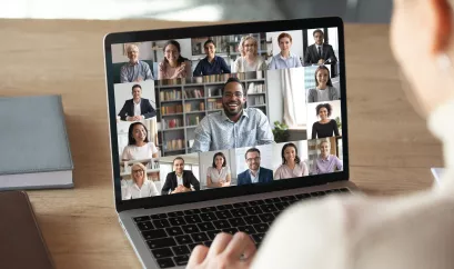 Person vor einem Laptopbildschirm, auf dem viele einzelne Menschen im Portrait zu sehen sind