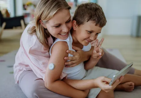 Mutter, die ihren Sohn mit Diabetes umarmt und zusammen ins Handy schauen