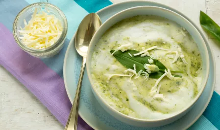 Die Bärlauchsuppe ist in einer Schale angerichtet und mit etwas Käse und einem Bärlauchblatt dekoriert. 